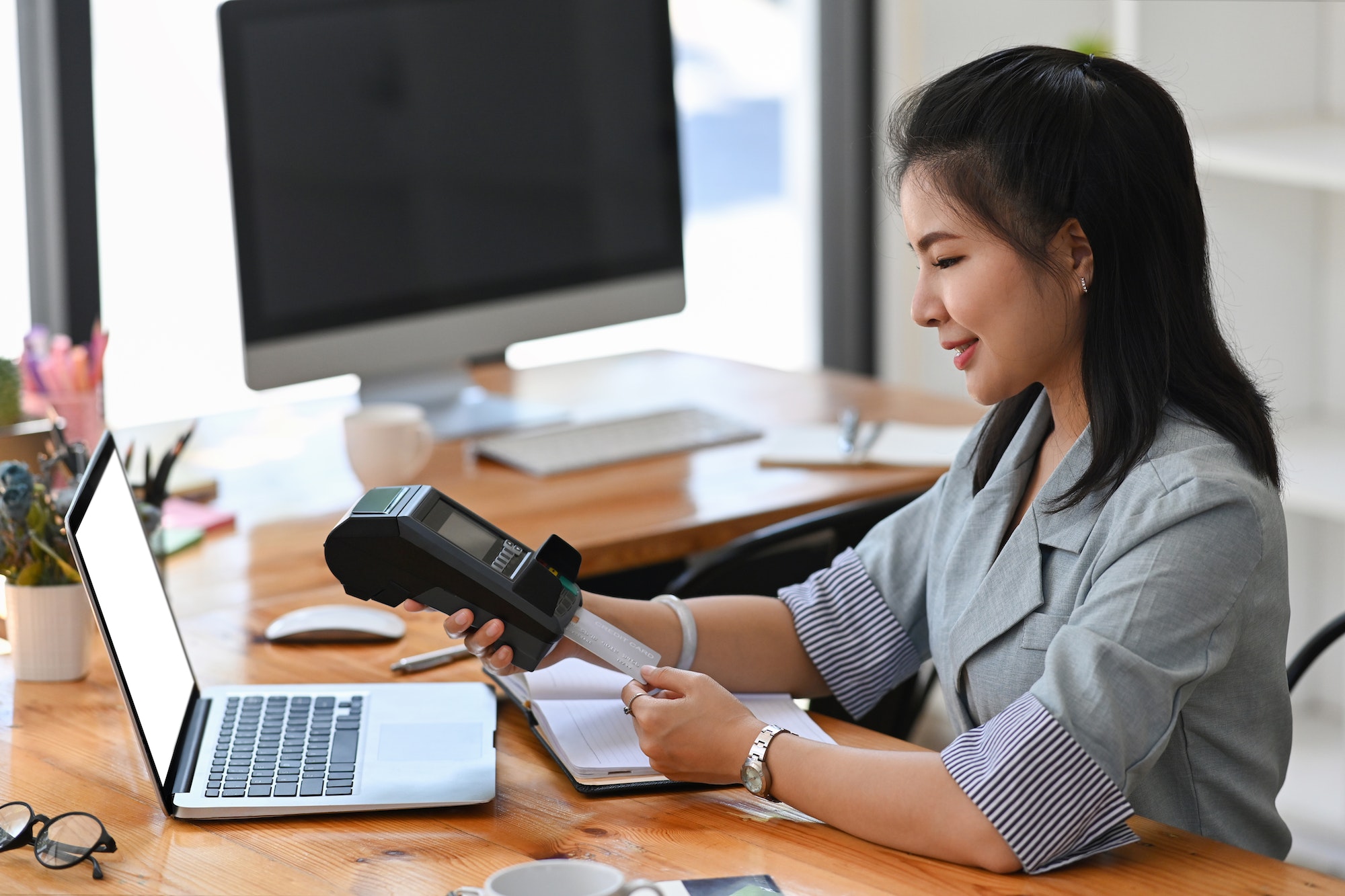 Smiling young woman swiping a credit card through terminal for payment.